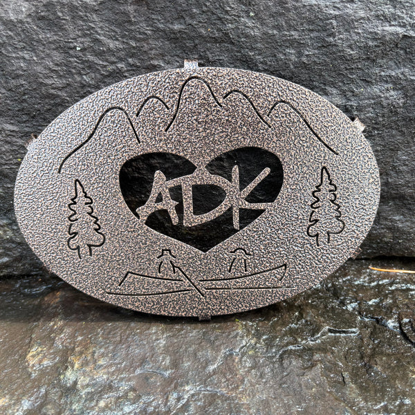 ADK in a heart with a mountain, trees and canoe scene on a copper penny metal trivet.
