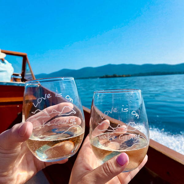 Two stemless glass wine glasses. Love is on Lake George text hand sand blasted over/under our Lake and mountain scene.
