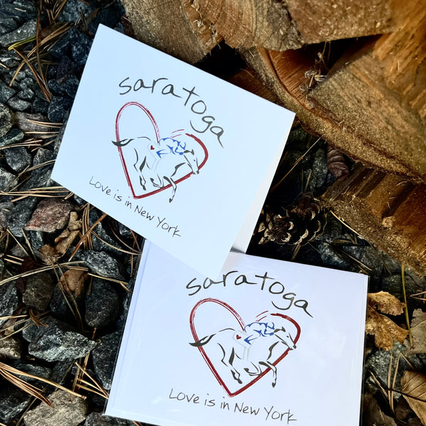 Red heart with a jockey dressed in blue riding a black horse. Saratoga Text arched over the top and Love is in New York under the graphic. Blank inside