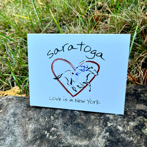 Red heart with a jockey dressed in blue riding a black horse. Saratoga Text arched over the top and Love is in New York under the graphic. Blank inside.