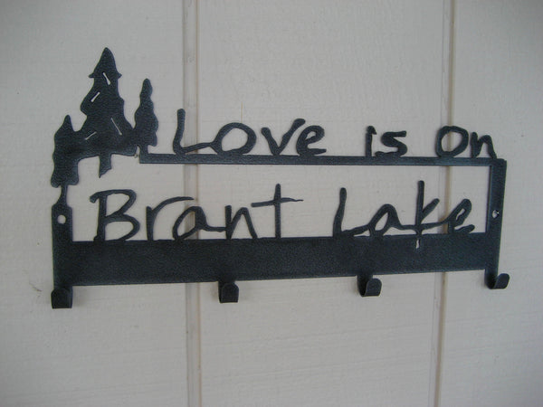 Two lines of text that include a grouping of three trees and Love is on Brant Lake. Graphite Black powder coated.
