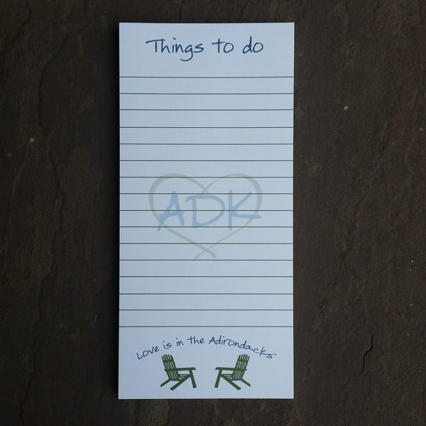ADK in a heart Silhouette in the middle of the notepad. Things to do text at the top of each sheet of paper. Love is in the Adirondacks text arched over two facing Adirondack chairs at the bottom of each sheet. White paper with ADK green text.