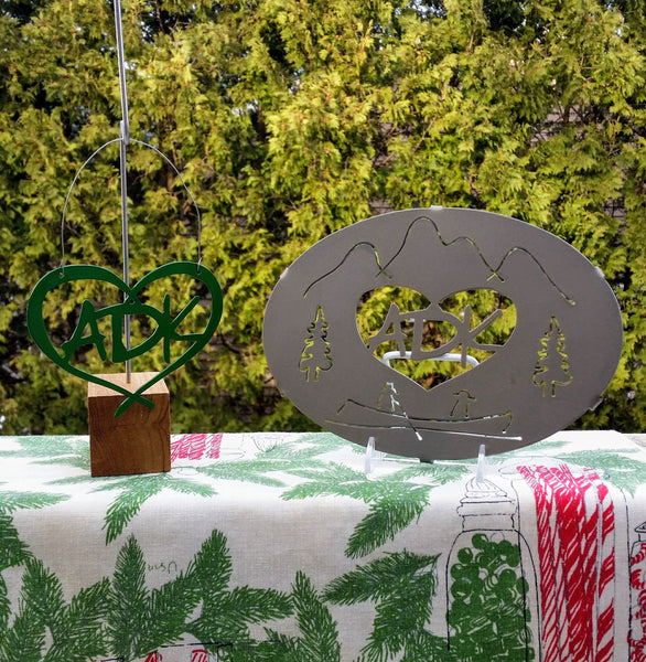ADK in a heart metal ornament with hanging wire. ADK in a heart hot plate with the mountainscape, ADK paddle boat and trees.