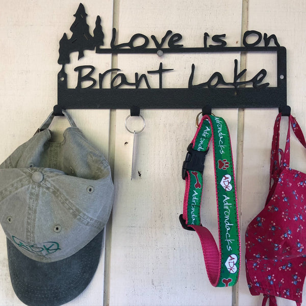 Two lines of text that include a grouping of three trees and Love is on Brant Lake. Graphite Black powder coated.