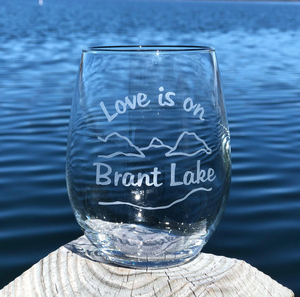 Clear stemless wine glass with a lake and mountain scene. Text reads Love is on Brant Lake
