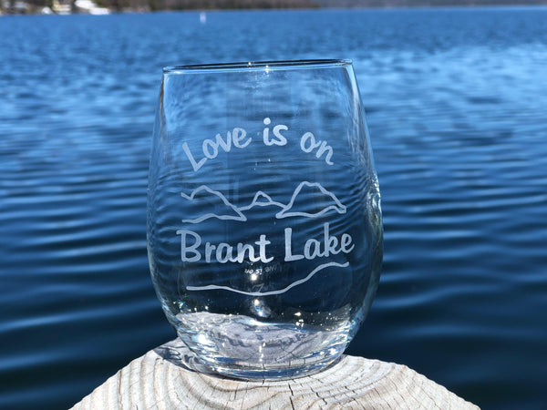 Clear stemless wine glass with a lake and mountain scene. Text reads Love is on Brant Lake