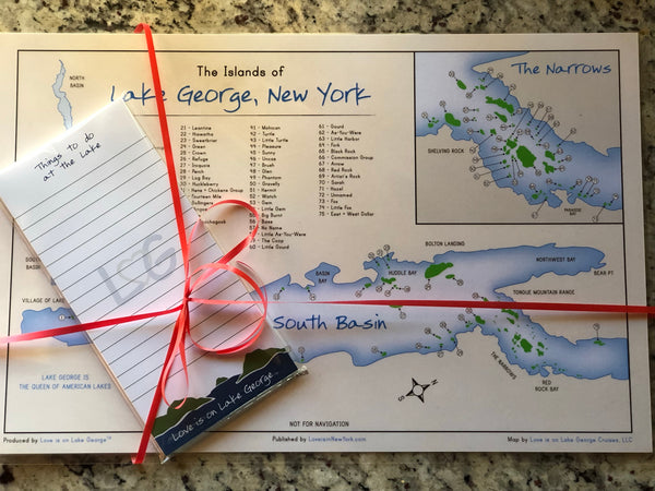 The Islands of Lake George laminated placemat. White background with the lake in blue, islands are green and the text is black. The notepad is white with blue lines,