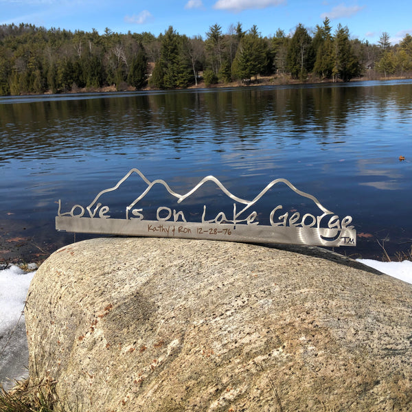 Love is on Lake George on a metal sign with the cutout of the Mountains.