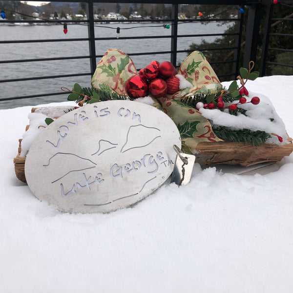 Love is on Lake George text on a lake/moutain scene stainless trivet. Paired with a key chain with the silhouette of Lake George on oneside and the Love is on Lake George text on the other side.