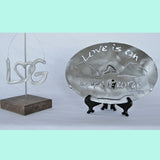 LheartG logo ornament.  Love is on Lake George text with the mountains and lake in between the text on a stainless trivet on a stand.