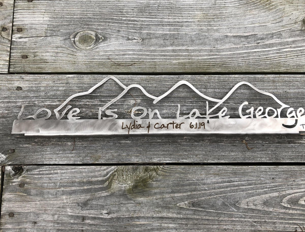 Love is on Lake George on a metal sign with the cutout of the Mountains.