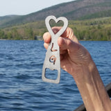Stainless bottle opener with a heart on top and the letter L above G, opener tab on the bottom.