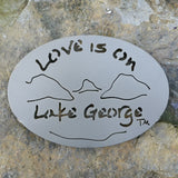 Text Love is on Lake George with the outline of the lake and surrounding Adirondack mountains; color is gold haze.