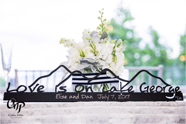 Love is on Lake George text on a metal sign with the cutout of the Mountains; graphite . It is pesonalized with Elise and Dan July 7, 2017te.
