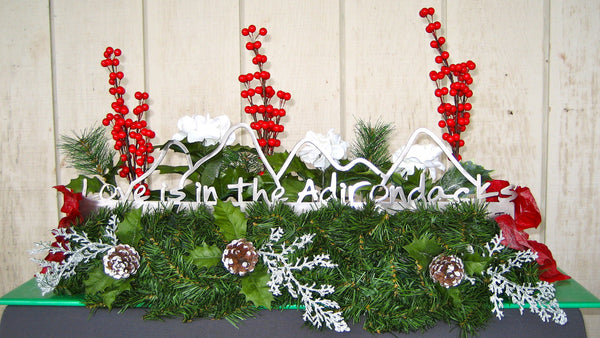 Love is in the Adirondacks text on the base with the outline of the Adirondack mountains cut out surrounded with greenery.