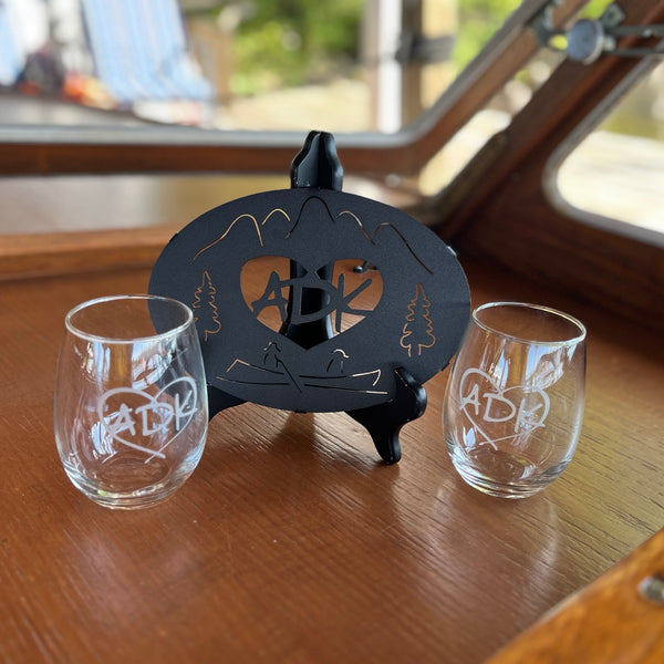 Black Metal trivet with our ADK in a heart logo paired with two clear stemless wine glasses.