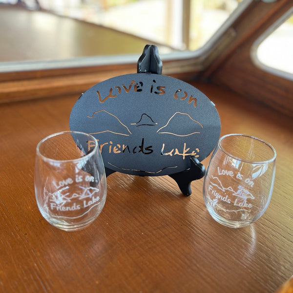 Love is on Friends Lake Black Metal trivet paired with two clear glass stemless wine glasses.