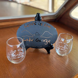 Twp Love is on Lake George clear stemless wine glass and a black metal trivet.