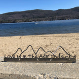 Love is in the Adirondacks text on a stainless steel shelf sitter inside the outline of a mountain scape. 