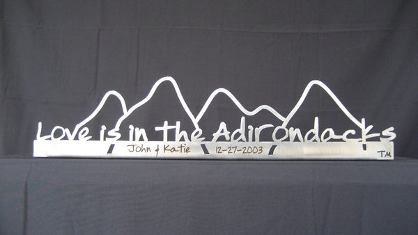 Love is in the Adirondacks text on the base of stainless sign inside the outline of the Adirondack mountain scape