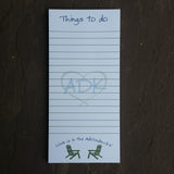 ADK in a heart Silhouette in the middle of the notepad. Things to do text at the top of each sheet of paper.  Love is in the Adirondacks text arched over two facing Adirondack chairs at the bottom of each sheet. White paper with ADK green text.