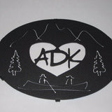 ADK in a heart with the Adirondack mountains, trees and guide boat.  It is powder coated graphite.  It is 8