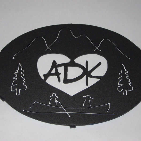 ADK in a heart with the Adirondack mountains, trees and guide boat.  It is powder coated graphite.  It is 8" x 6".