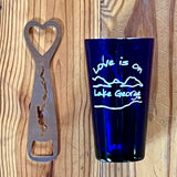 iLove is on Lake George text over our mountain/lake scene printed in white on a blue pint glass. Stainless Bottle Opener with the silhouette of Lake George cutout.