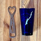 Silhouette of Lake George printed in white on a blue glass. Stainless Bottle Opener with the silhouette of Lake George cutout.
