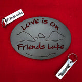 Love is on Friends Lake Text arched above and below a mountain/lake scene on a black metal trivet.  It is paired with a stainless two-sided key chain with "Friends Lake" on one side and the silhouette of Friends Lake on the other side.