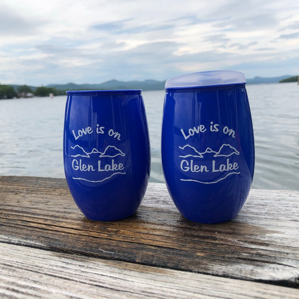 A pair of Love is on Glen Lake Text in white on a blue plastic cup with the lake and mountain scene.