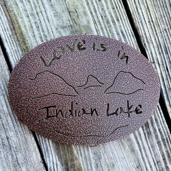 Love is in Indian Lake text  cut out  with our Lake and mountain scene on a copper penny metal trivet.