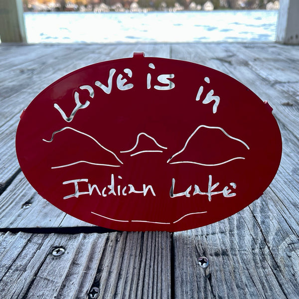 Love is in Indian Lake text  cut out  with our Lake and mountain scene on a red metal trivet.