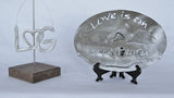 LheartG logo ornament. Love is on Lake George text with the mountains and lake in between the text on a stainless trivet on a stand.