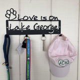 Love is on Lake George text on a wall mount with 4 hooks to hang things; paw outline in the upper left corner.