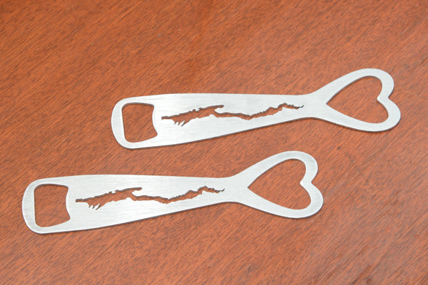 A pair of stainless metal bottle opener with a heart cut out on the top, silhouette of Lake George cut out in the body, and bottle opener cut out at the bottom.