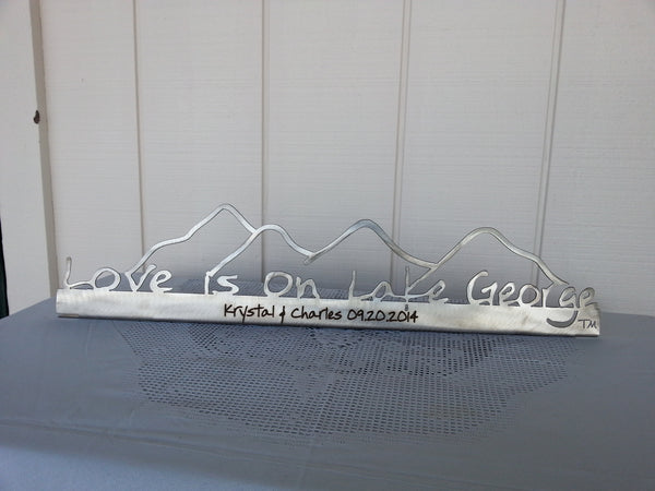 Love is on Lake George on a metal sign with the cutout of the Mountains.