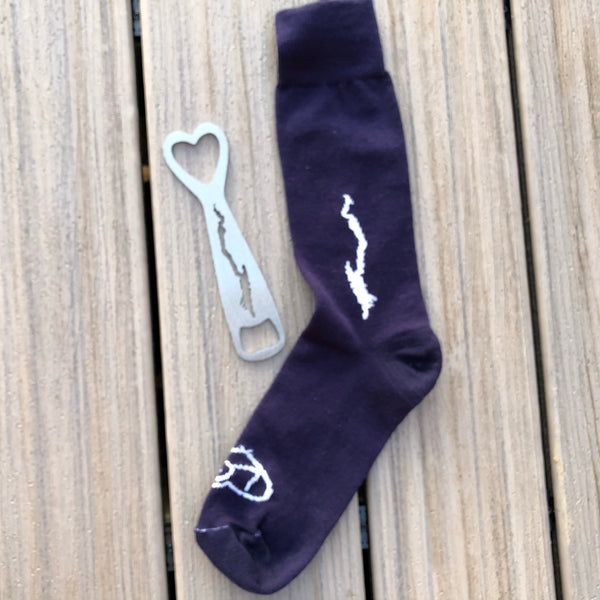 Stainless steel silhouette of Lake George bottle opener and a pair of navy blue unisex socks with the Silhouette of Lake George embroidered in white on the shin of your leg. 