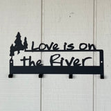Love is on the Rivert text on a black metal foor hook wall mount with some ADK trees.