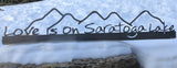 Stainless metal sign with mountains and the text "Love is on Saratoga Lake under the mountains.
