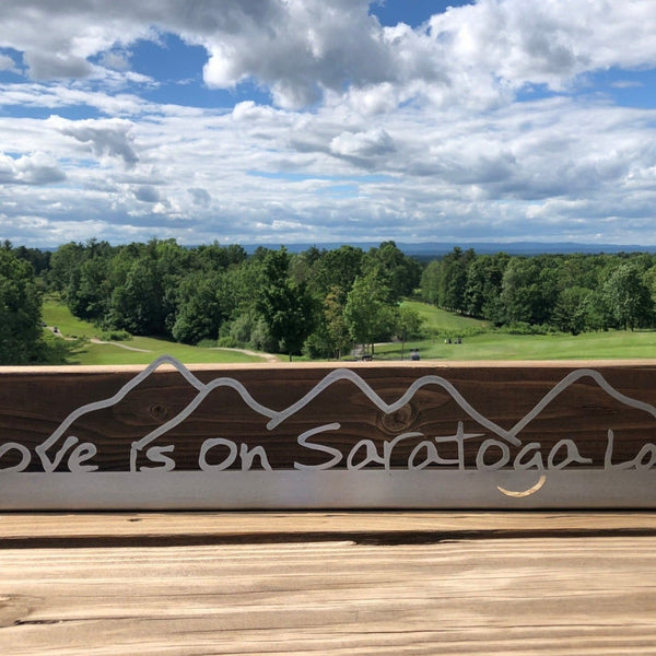 Love is on Saratoga Lake text on a metal sign with mountains.