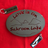 Love is on Schroon Lake text over/under a lake/mountain scene on a black metal trivet.  It is paired with a stainless Schroon Lake keychain  that has the silhouette of the lake on one side.