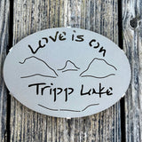 Love is on Tripp Lake text over our cutout  Lake and Mountain scene on a gold haze metal trivet.
