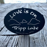 Love is on Tripp Lake text over our cutout  Lake and Mountain scene on a black metal trivet.