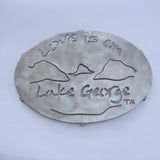 Love is on Lake George text above and below a lake and mountain scene on a stainless trivet.